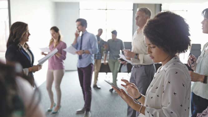 People in a group standing around holding papers or phones and listening to a presenter
